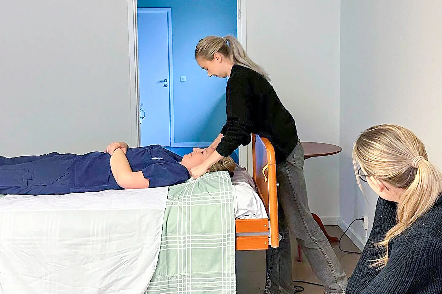 Utbildning i klinisk introduktion där en instruktör visar en övning på en person som ligger i sängen.